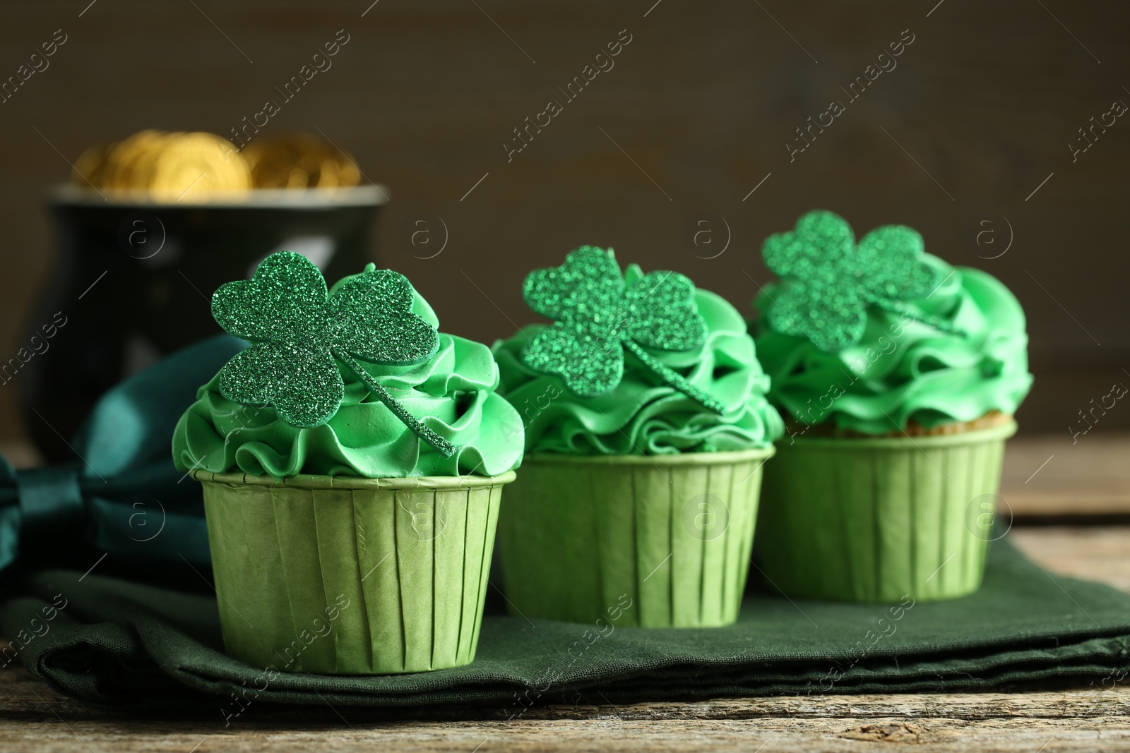 Photo of St. Patrick's day party. Tasty cupcakes with clover leaf toppers and green cream on wooden table, closeup