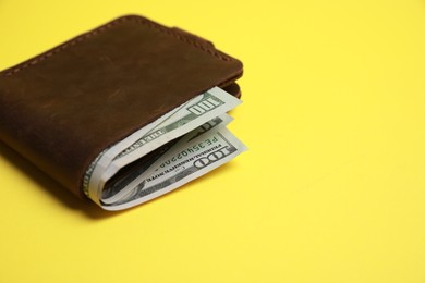 Photo of Stylish brown leather wallet with dollar banknotes on yellow background, closeup. Space for text