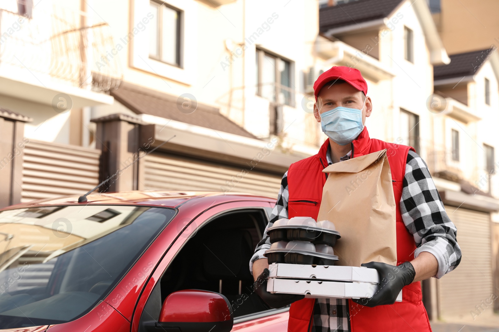 Photo of Courier in protective mask and gloves with orders near car outdoors. Food delivery service during coronavirus quarantine