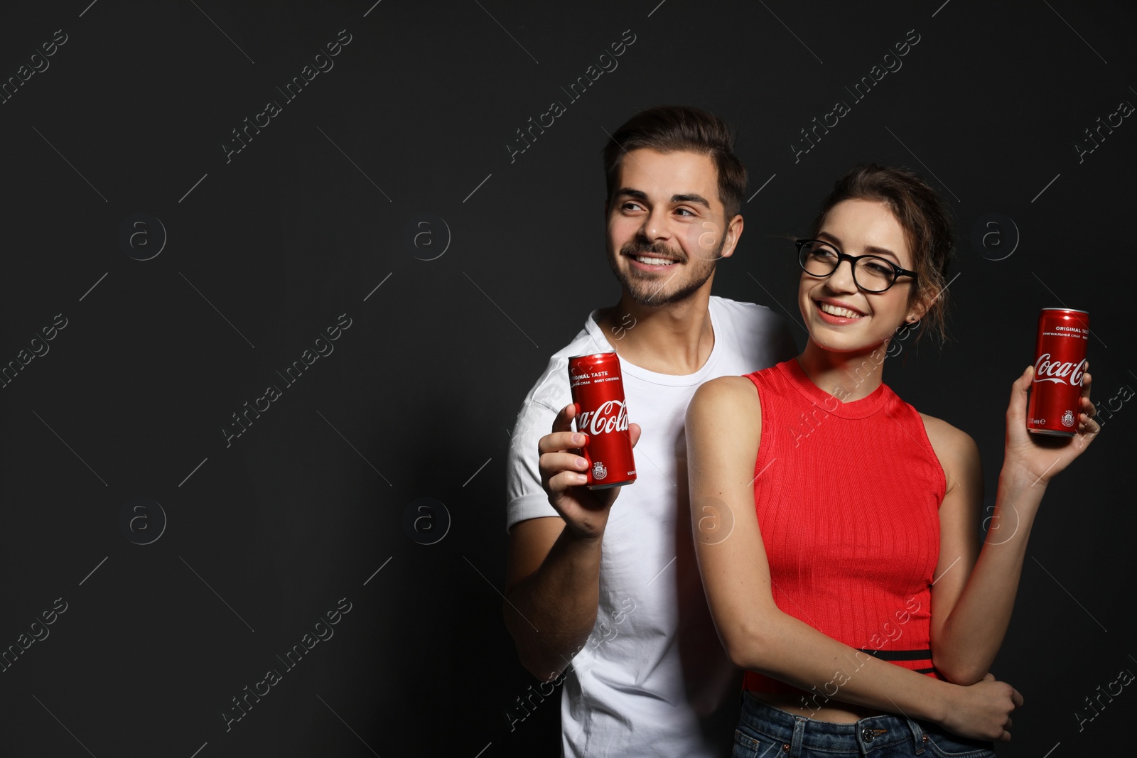 Photo of MYKOLAIV, UKRAINE - NOVEMBER 28, 2018: Young couple with Coca-Cola cans on dark background, space for text