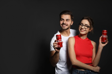 Photo of MYKOLAIV, UKRAINE - NOVEMBER 28, 2018: Young couple with Coca-Cola cans on dark background, space for text