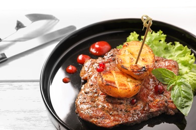 Plate with tasty grilled meat and potatoes on table, closeup