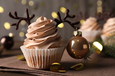 Photo of Tasty cupcake with chocolate reindeer antlers and Christmas bauble on table, closeup