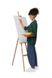 Photo of Young woman painting on easel with canvas against white background
