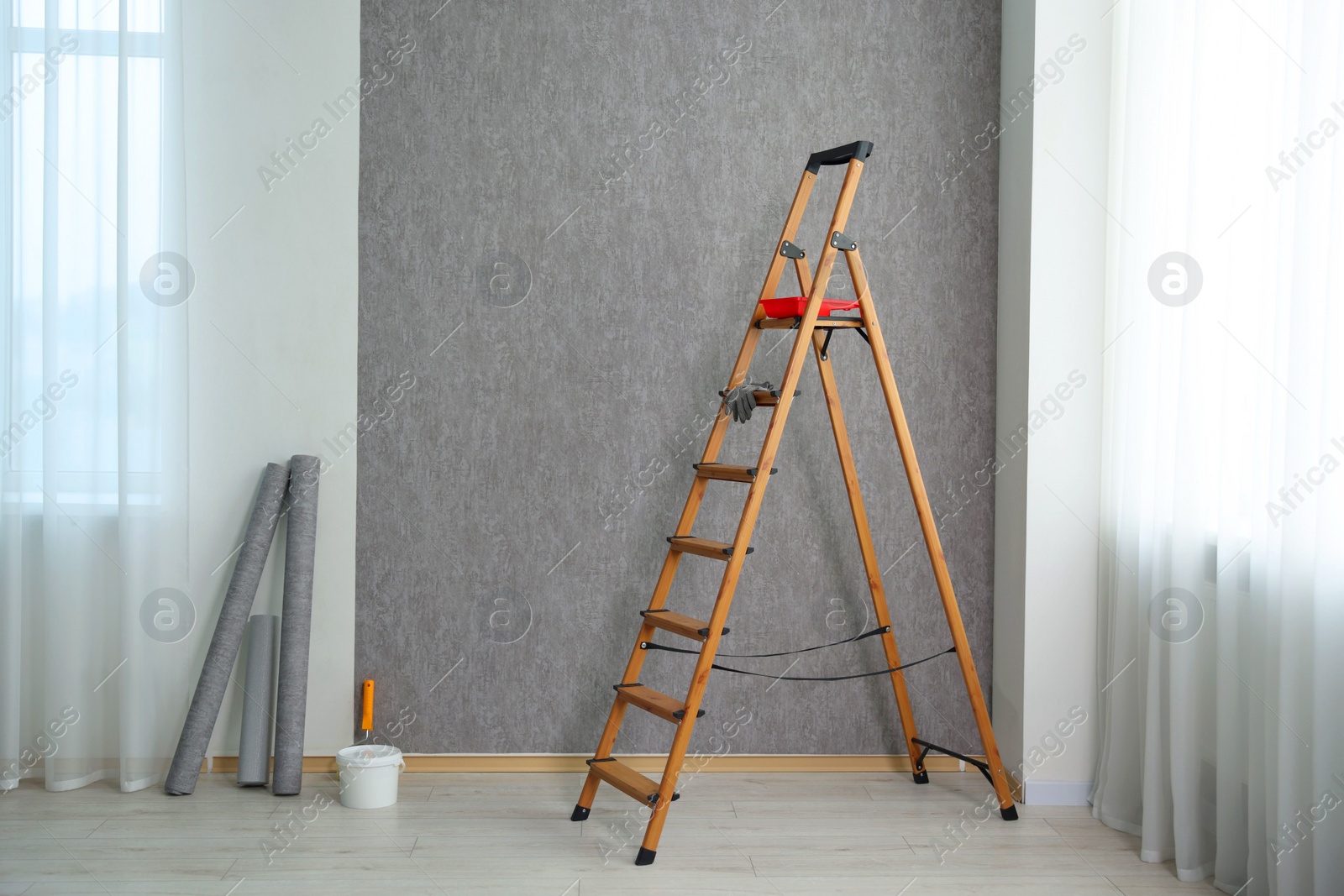 Photo of Wallpaper rolls, bucket with glue and wooden ladder in room