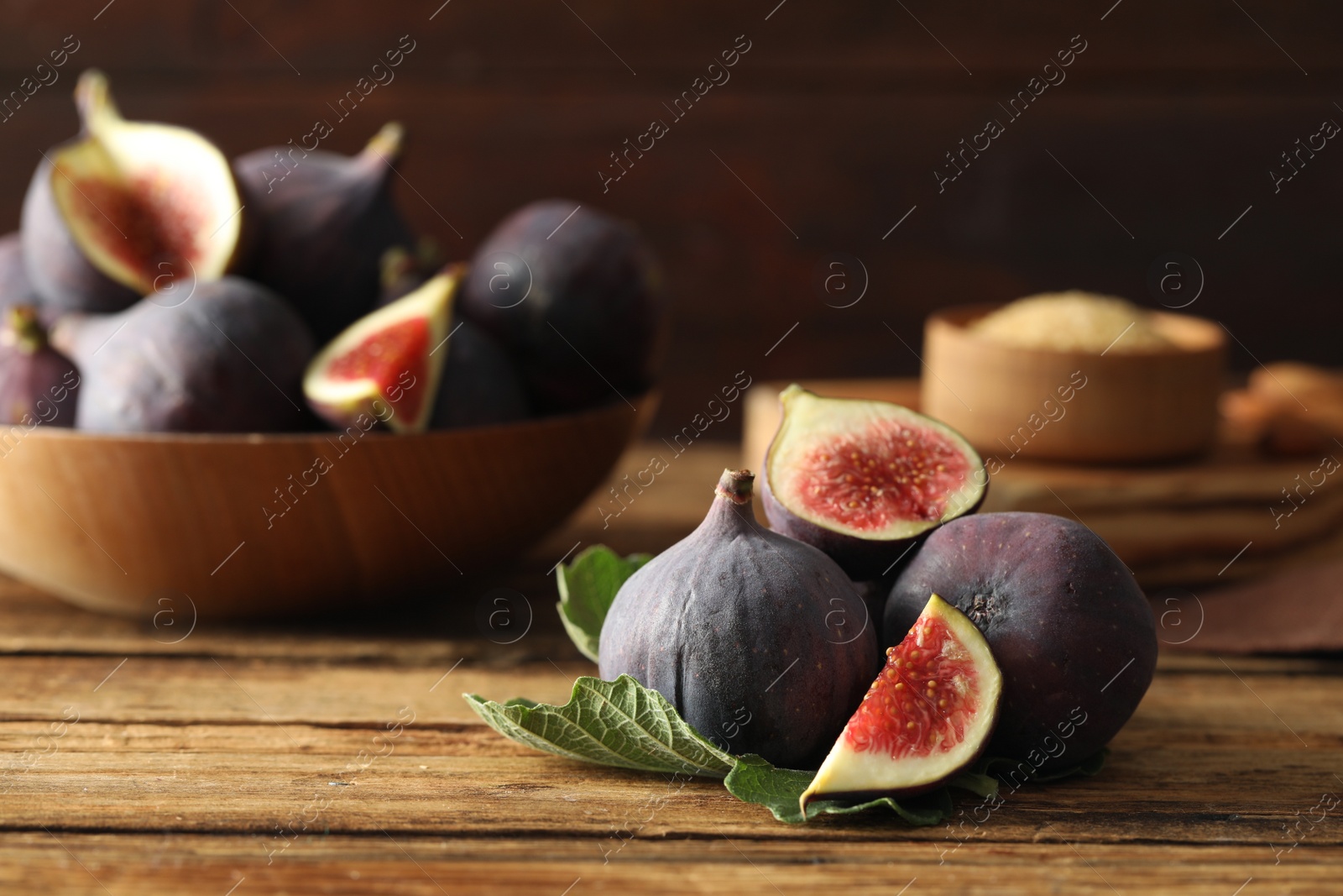 Photo of Whole and cut tasty fresh figs with green leaf on wooden table