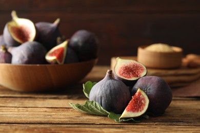 Photo of Whole and cut tasty fresh figs with green leaf on wooden table