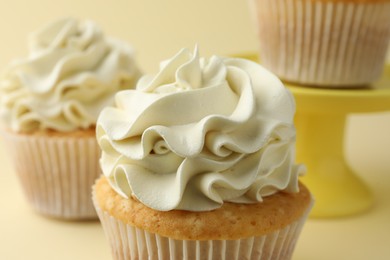 Photo of Tasty vanilla cupcakes with cream on pale yellow background, closeup