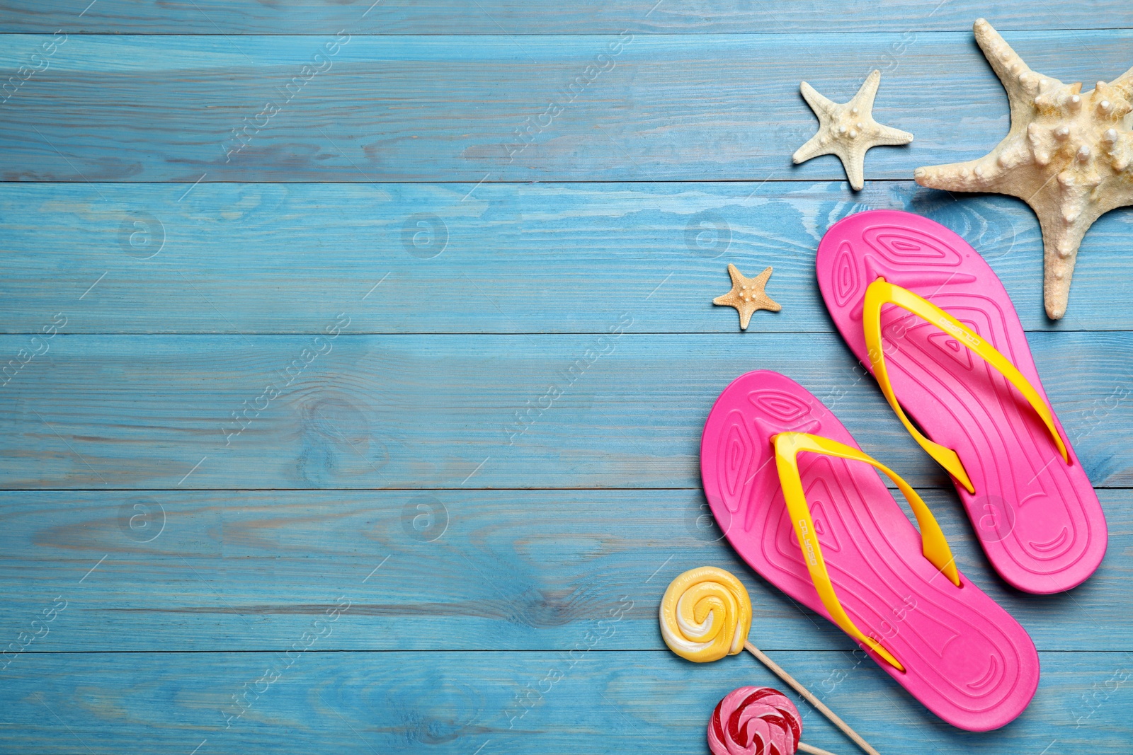 Photo of Stylish flip flops, starfish and lollipops on light blue wooden background, flat lay. Space for text