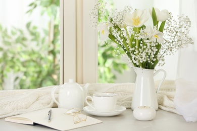 Beautiful fresh flowers, hot coffee and notebook on window sill indoors