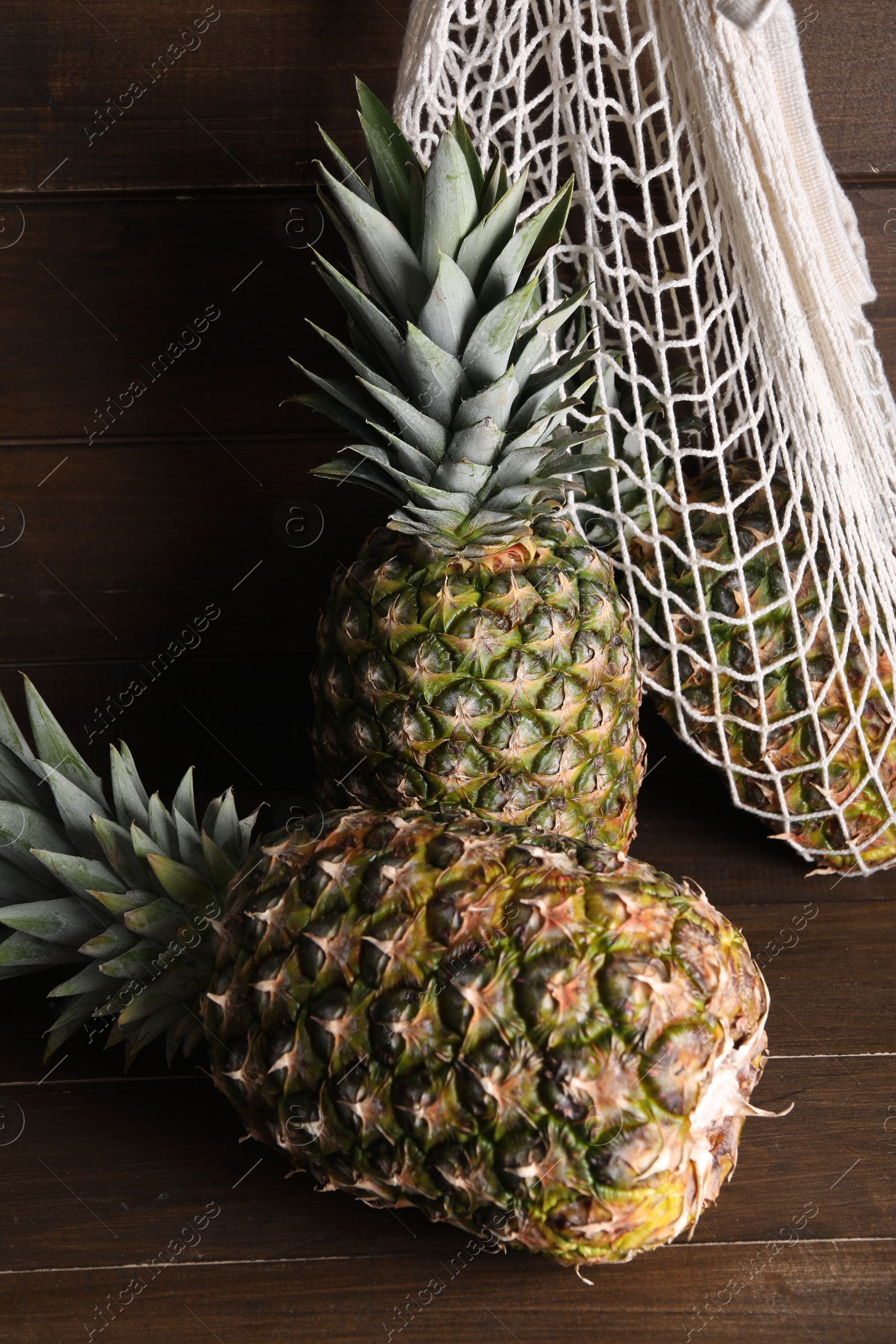 Photo of Whole ripe pineapples and net bag on wooden table