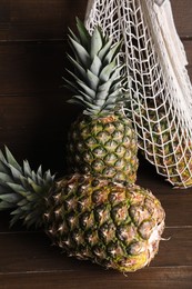 Whole ripe pineapples and net bag on wooden table
