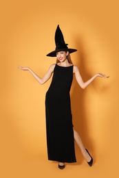 Beautiful woman wearing witch costume for Halloween party on yellow background