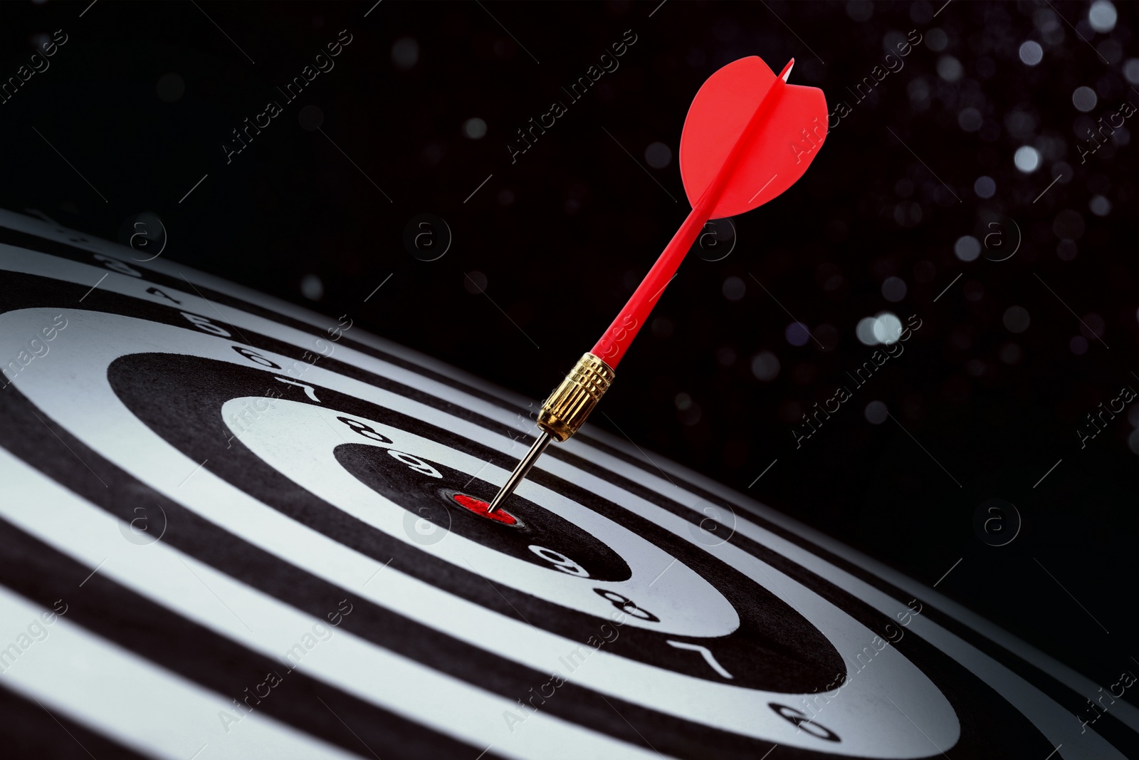Image of Dart board with red arrow hitting target against black background, bokeh effect