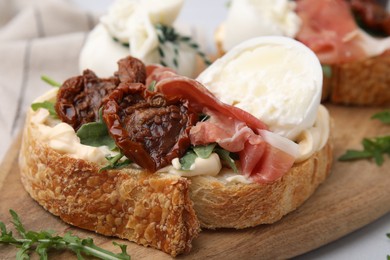 Delicious sandwich with burrata cheese, ham and sun-dried tomatoes served on table, closeup
