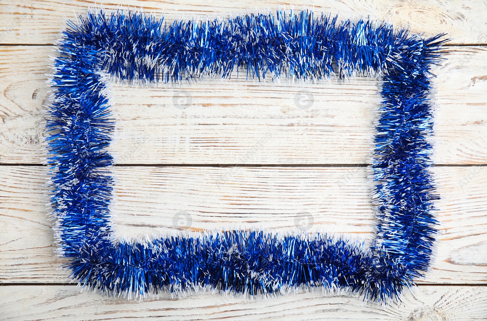 Photo of Frame of blue tinsel on white wooden background, top view. Space for text