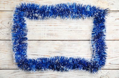 Frame of blue tinsel on white wooden background, top view. Space for text