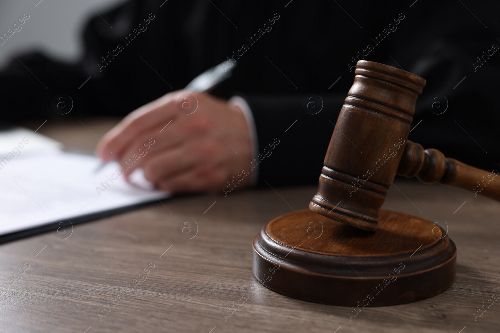 Photo of Judge with gavel writing in papers at wooden table, closeup