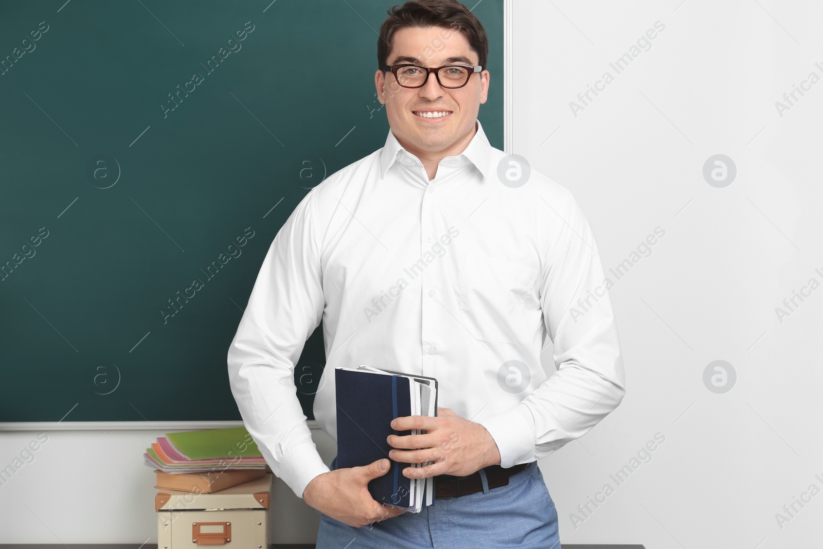 Photo of Portrait of male teacher with notebooks near chalkboard in classroom