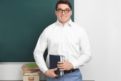 Photo of Portrait of male teacher with notebooks near chalkboard in classroom