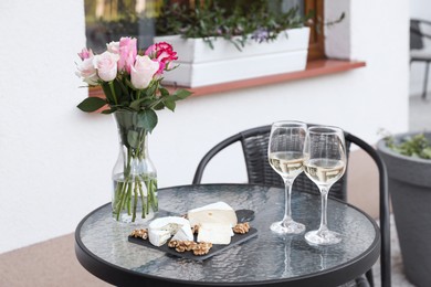 Photo of Vase with roses, glasseswine and food on glass table near house on outdoor terrace