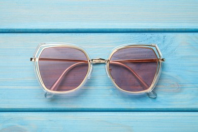 Photo of New stylish sunglasses on turquoise wooden table, top view