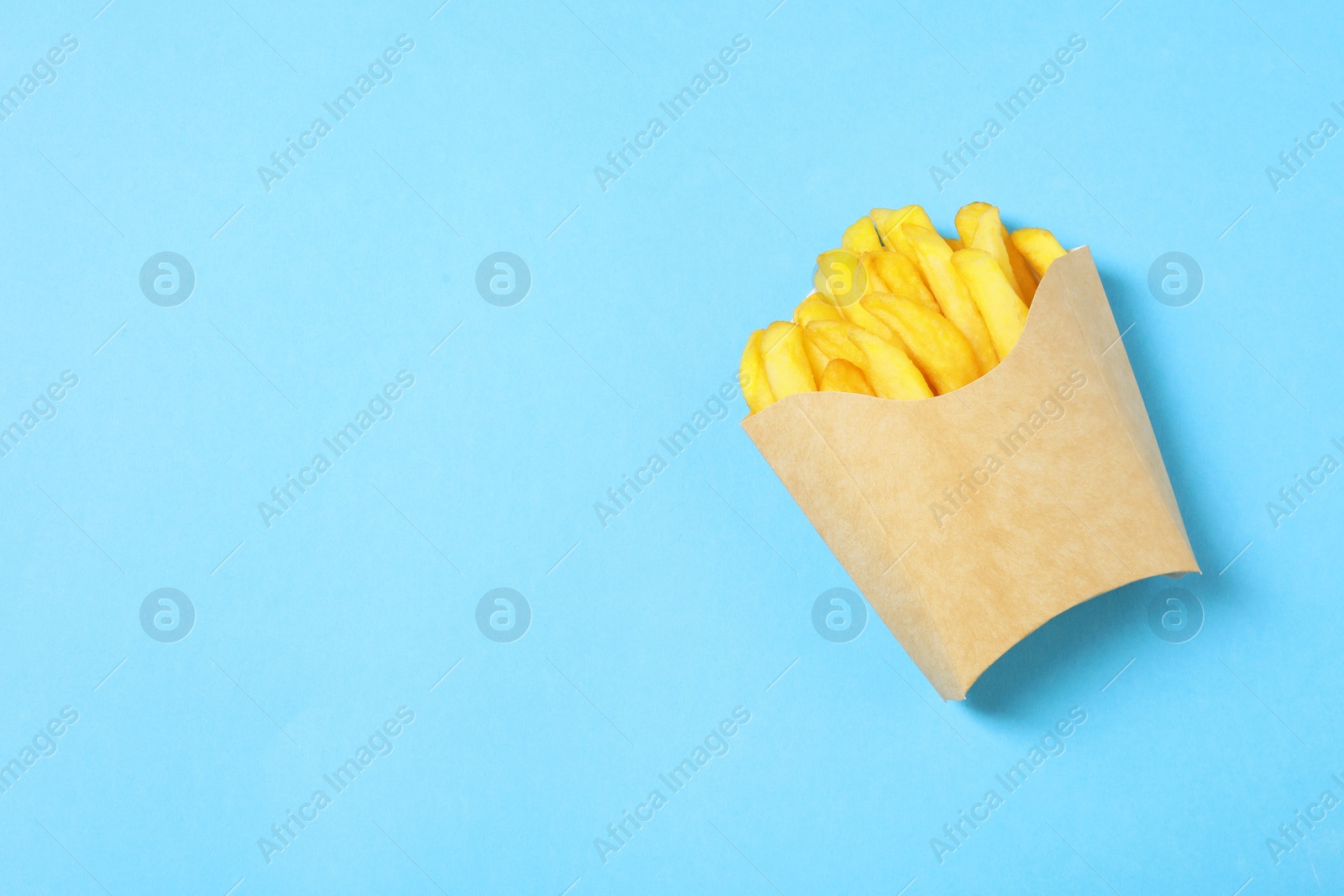 Photo of Paper cup with French fries on light blue table, top view. Space for text