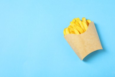 Paper cup with French fries on light blue table, top view. Space for text