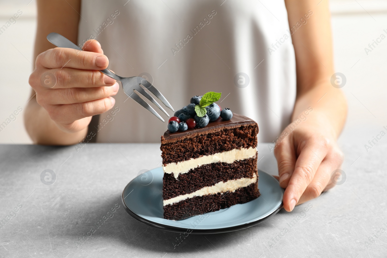 Photo of Woman with slice of chocolate sponge berry cake at table, closeup