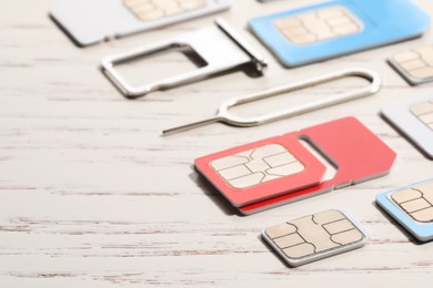 Photo of Different SIM cards, ejector and tray on white wooden background, closeup