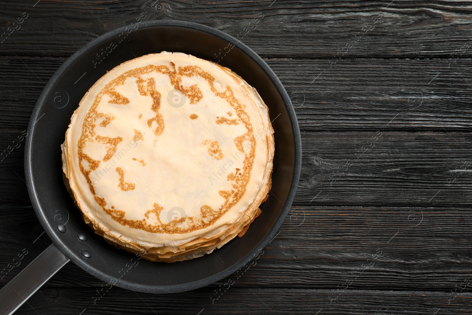 Photo of Frying pan with thin pancakes on wooden background, top view