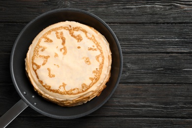 Frying pan with thin pancakes on wooden background, top view