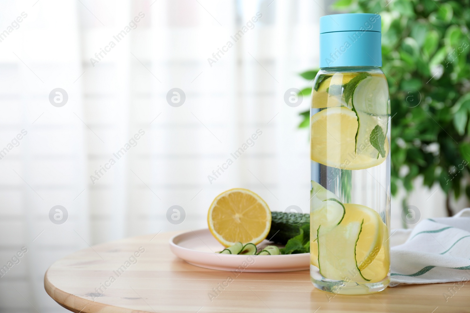 Photo of Bottle of refreshing water with cucumber, lemon and mint on wooden table indoors. Space for text