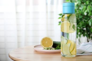 Bottle of refreshing water with cucumber, lemon and mint on wooden table indoors. Space for text