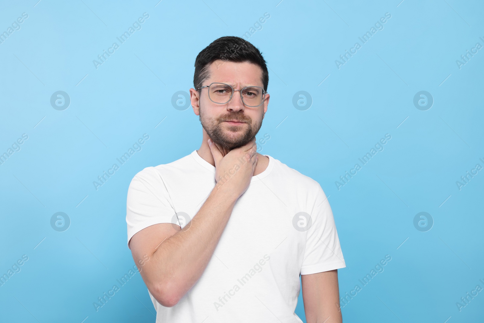 Photo of Man suffering from sore throat on light blue background