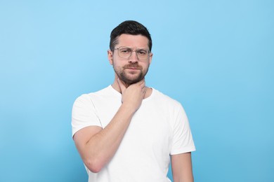 Man suffering from sore throat on light blue background
