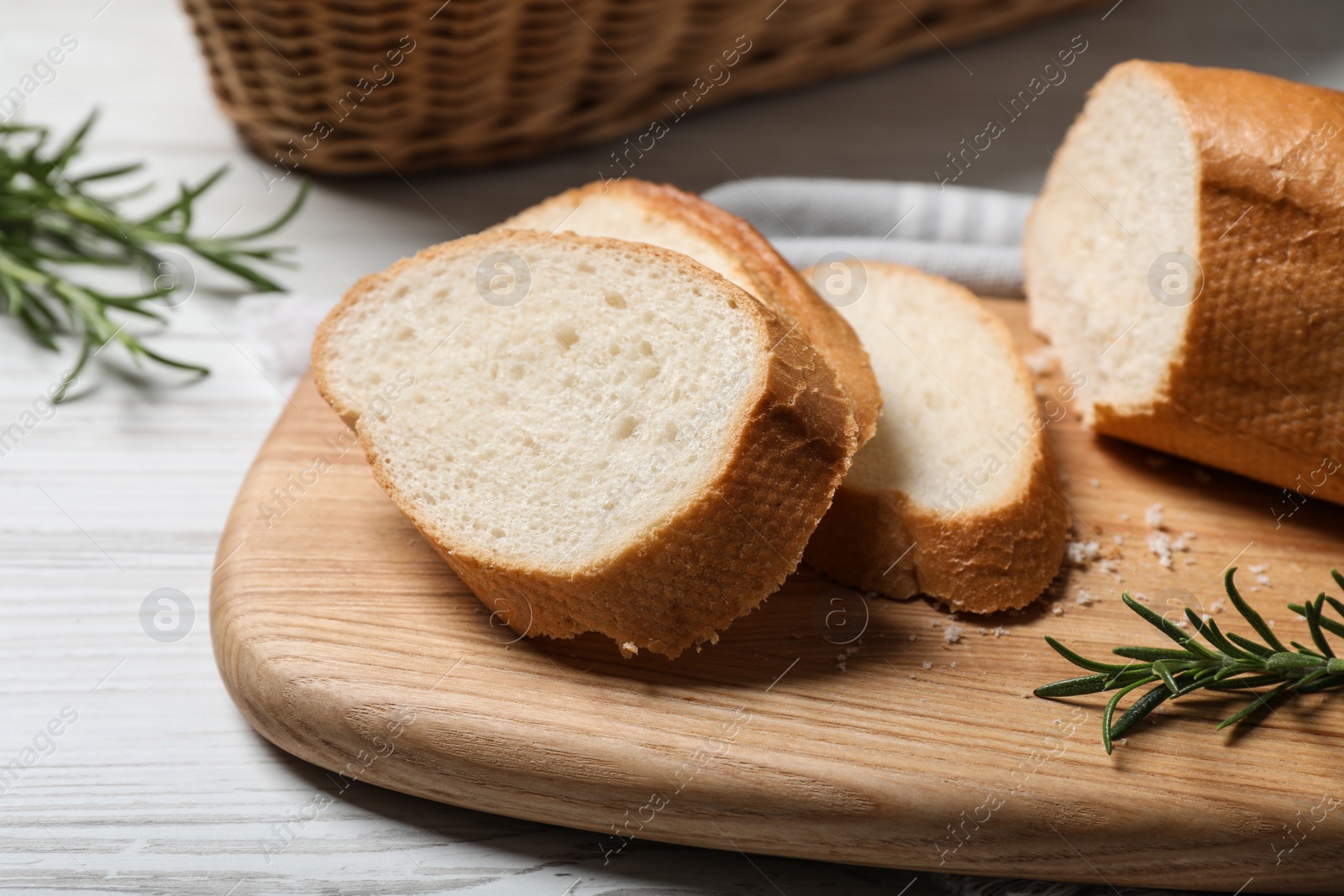 Photo of Cut tasty baguette with rosemary on white wooden table, closeup