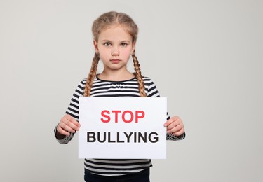 Girl holding sign with phrase Stop Bullying on light grey background