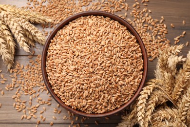 Photo of Wheat grains in bowl and spikes on wooden table, flat lay