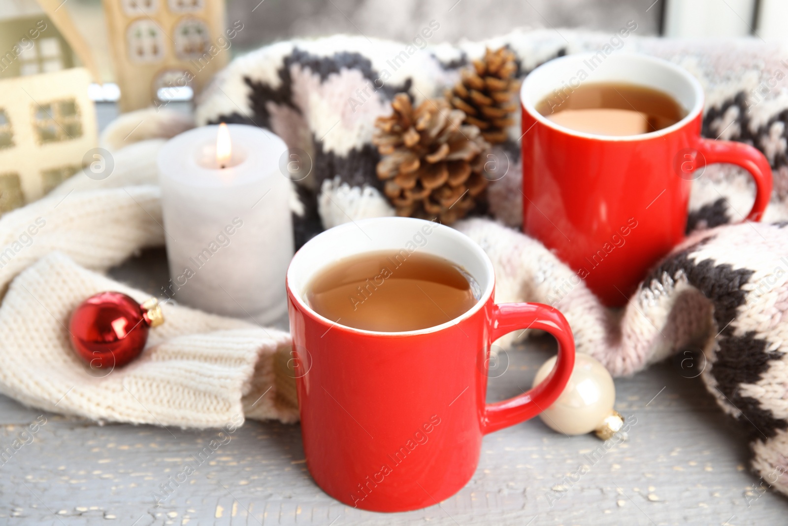 Photo of Cups of hot winter drink with scarf on window sill indoors