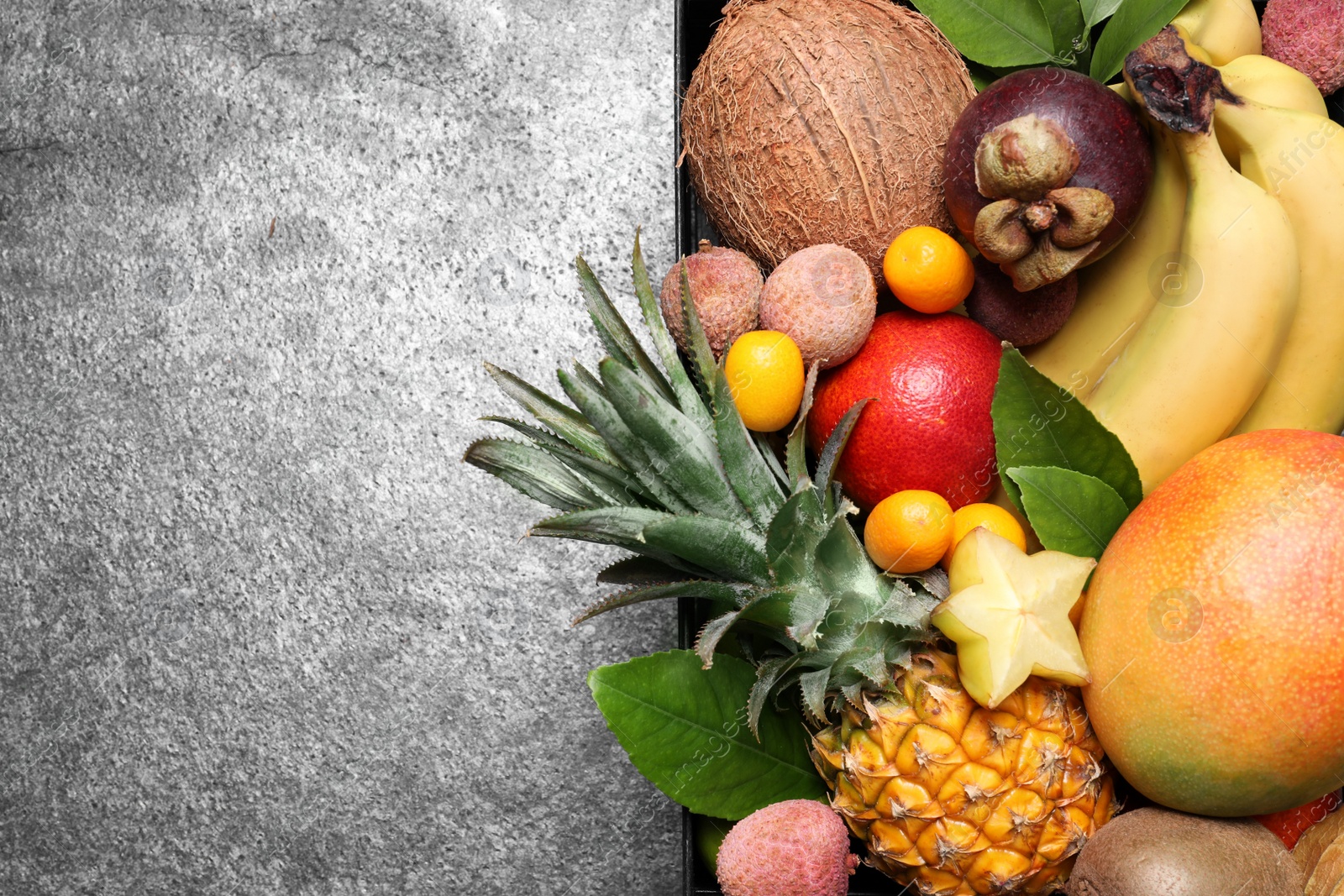 Photo of Different tropical fruits in wooden box on grey background, top view. Space for text