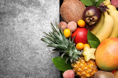 Different tropical fruits in wooden box on grey background, top view. Space for text