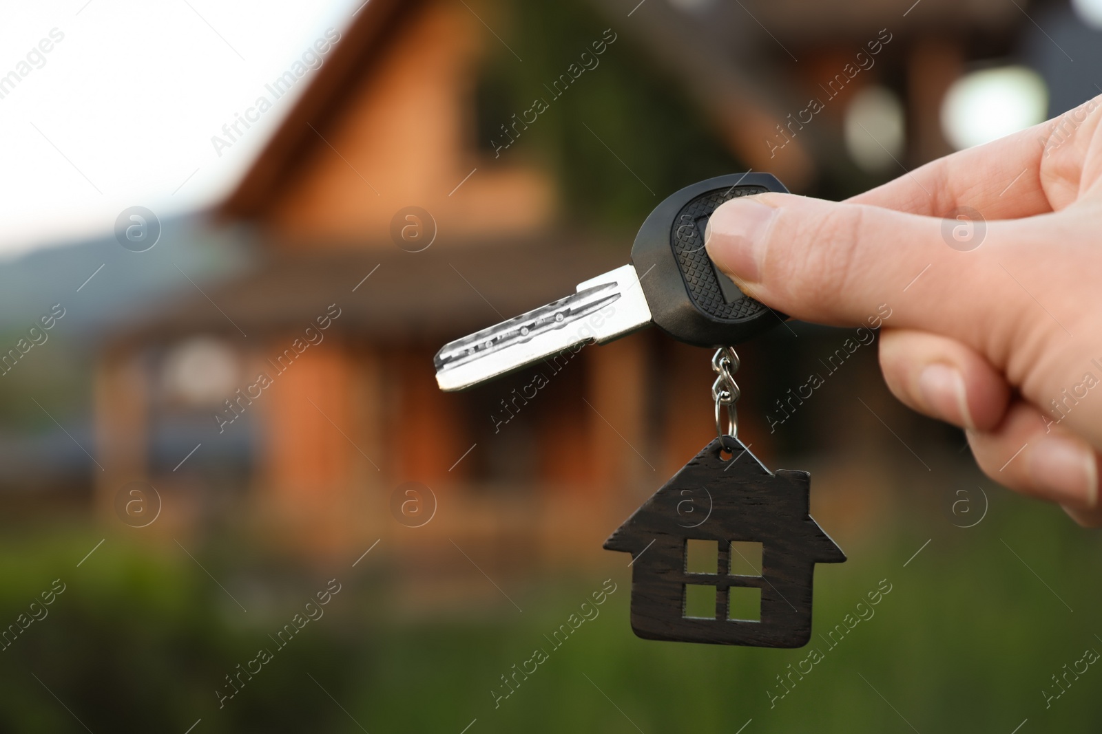 Photo of Real estate agent holding key and blurred house on background. Focus on hand