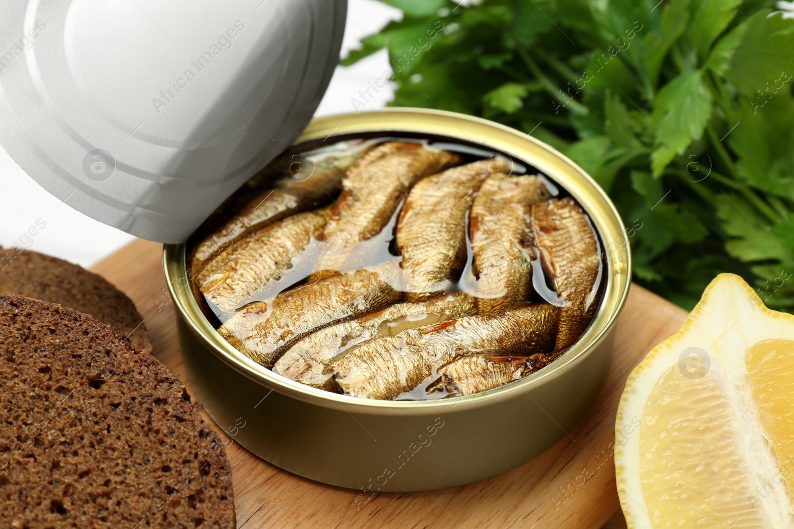 Photo of Canned sprats, lemon and bread on wooden board, closeup