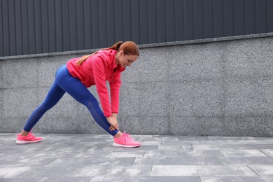 Beautiful woman in gym clothes doing exercises on street, space for text