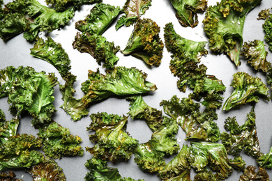 Photo of Tasty baked kale chips on grey table, flat lay