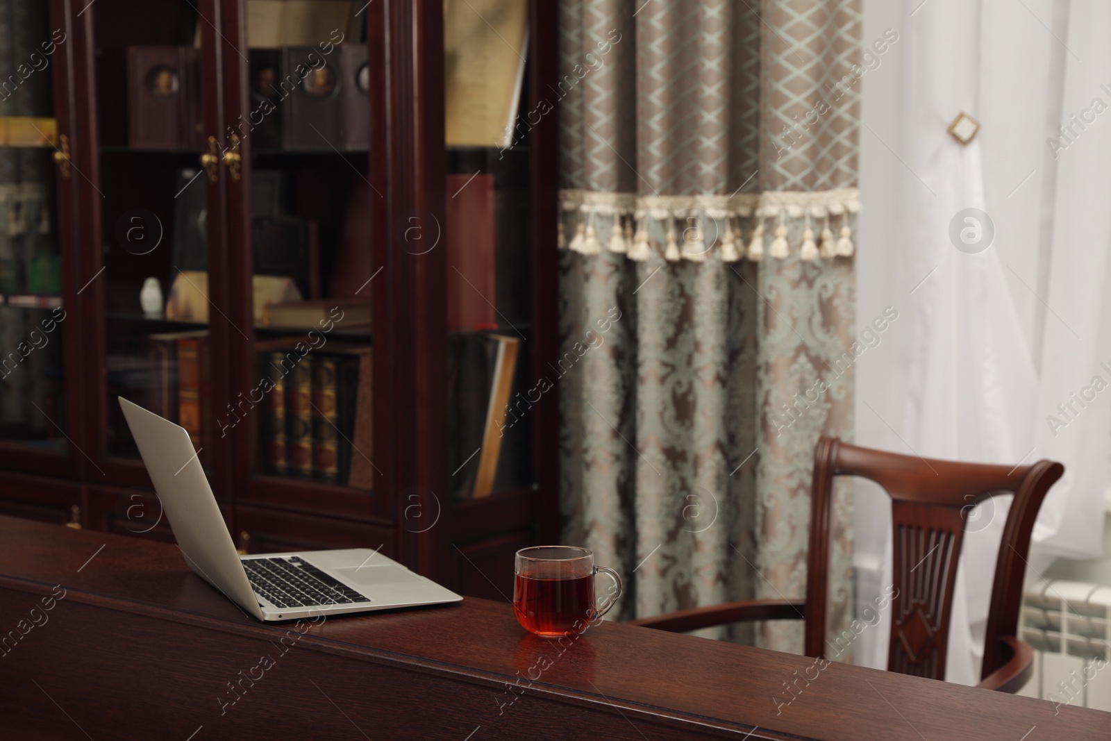 Photo of Laptop and cup of tea on wooden table in library reading room