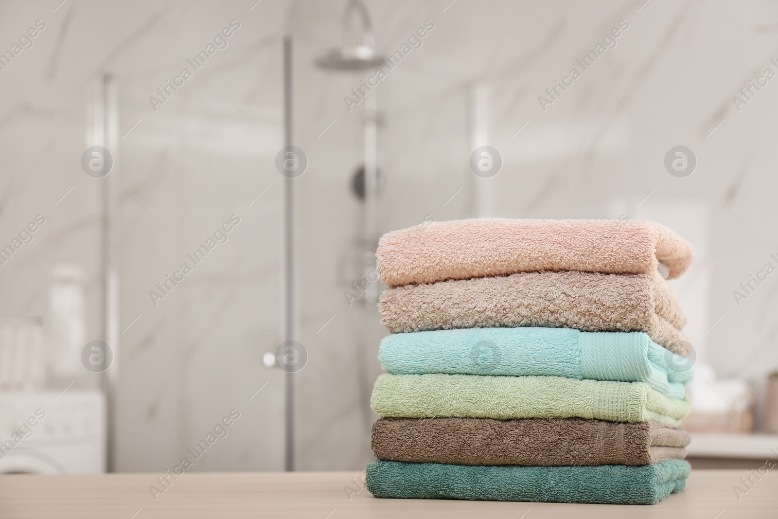 Photo of Stack of fresh towels on wooden table in bathroom. Space for text