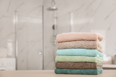 Photo of Stack of fresh towels on wooden table in bathroom. Space for text