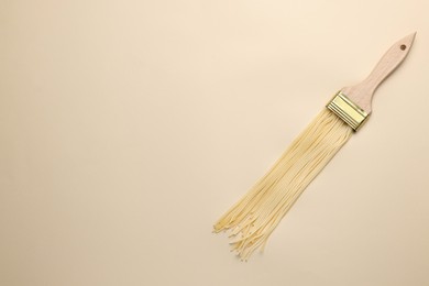 Photo of Brush painting with spaghetti on beige background, top view. Space for text. Creative concept